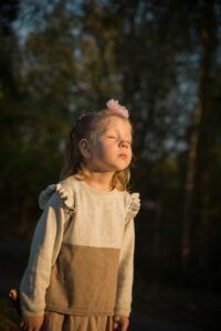 A young girl with eyes closed basking in the warm evening sunlight in a forest setting.