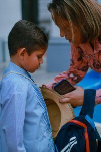 A mother helps her young son with his backpack, preparing for a school day.