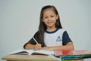 A young girl sitting at a desk, studying with open books and smiling.