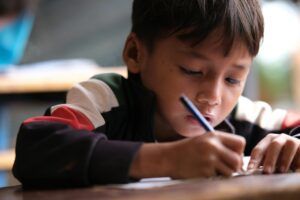 A young boy intently writing in a classroom setting, concentrating on his task.