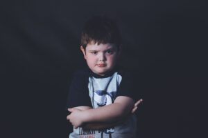 A thoughtful young boy with crossed arms against a dark background, expressing introspection and emotion.